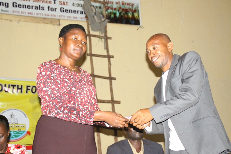 Hon. Sseninde hand over Shs.500,000 to Entebbe Youth Leader Tibamanya Robert at the Cinema Hall in Entebbe.